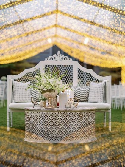A beautiful white diwan sits before the glittering sangeet stage, offering a regal photo opportunity. The entire setup is a blend of traditional Indian craftsmanship and modern event design.