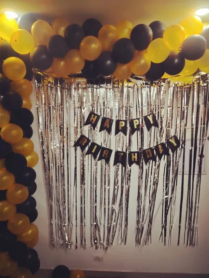 A black and yellow balloon arch against a silver tinsel curtain for a home birthday party.