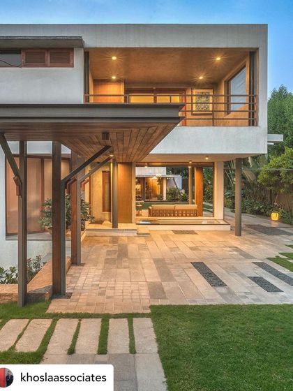 The entrance of a villa at dusk, showing the integration of the carport with the garden. The design uses pathways and low planting to create a seamless flow from the driveway to the front door.