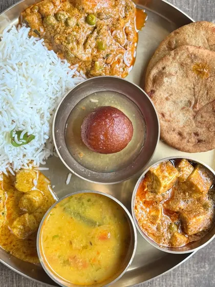 A complete vegetarian thali with two types of paneer, dal, rice, roti, and a gulab jamun for dessert.