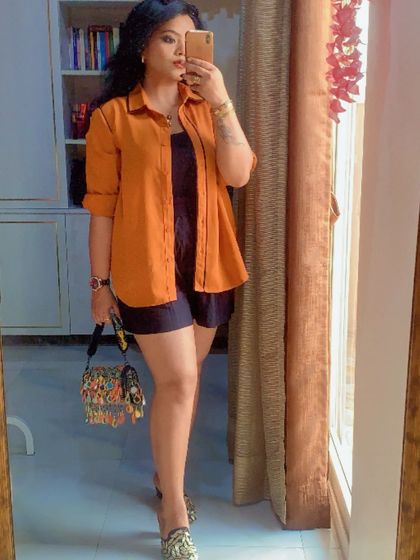 A mirror selfie capturing a chic layered look with an orange shirt over a black base.