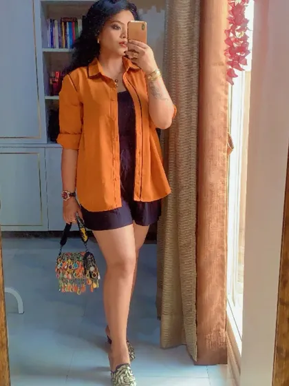 A mirror selfie capturing a chic layered look with an orange shirt over a black base.