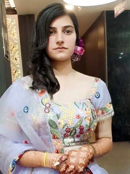 A full-length view of the Roka ceremony look. The light makeup and floral hairstyle perfectly match her embroidered pastel lehenga and henna-adorned hands.