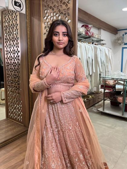 A close-up of the model in the peach lehenga, highlighting the intricate work on the full-sleeve blouse.
