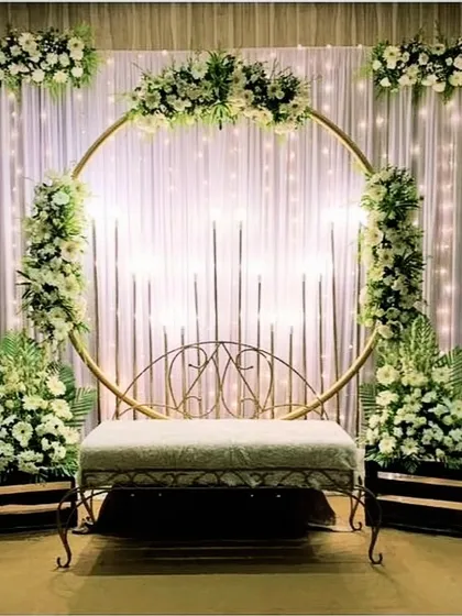 A simple and charming stage decoration for just 12,000. This setup uses a circular golden frame with white flowers and fairy lights, ideal for smaller functions or home events.