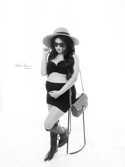A fun and fashionable black and white portrait with a playful attitude. The styling with the hat, sunglasses, and boots shows that maternity photography can be trendy and full of personality.