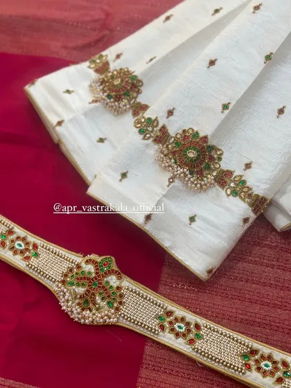 An elegant white blouse with red and green temple jewellery embroidery, paired with a matching waist belt.