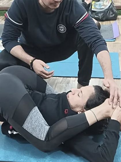 An instructor provides a final adjustment to help a student settle into Yoganidrasana, a very advanced posture.