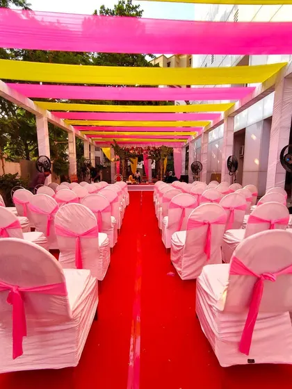 For larger gatherings, we can transform outdoor spaces with vibrant, traditional decor. Here, we used bright pink and yellow fabric drapes to create a festive canopy over the guest seating area for a naming ceremony.