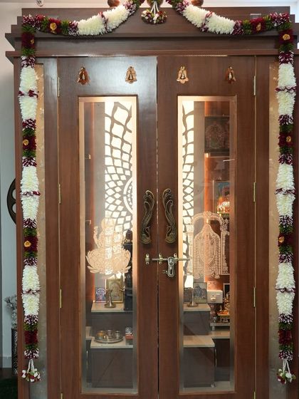A beautifully decorated wooden pooja mandir with glass doors, etched with sacred symbols. The unit is ready for a housewarming ceremony.