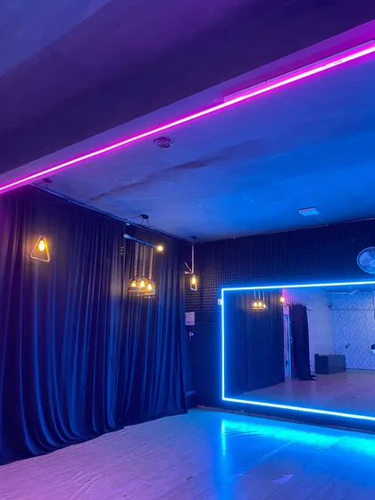 Welcome to our space. The studio is designed with bright, energizing neon lights, full wall mirrors for checking form, and professional-grade wooden floors to create the perfect training environment.