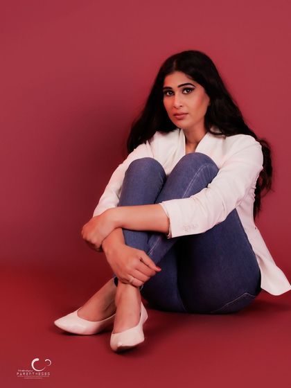 A gentle and introspective pose. The way she hugs her knees creates a sense of comfort and vulnerability against the bold red backdrop.