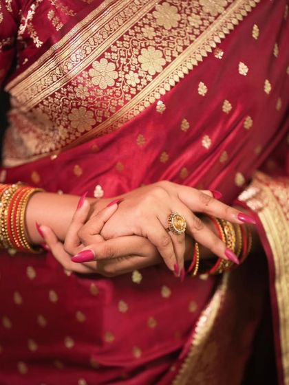 A detail shot focusing on the bride's hands, adorned with bangles and a statement ring, resting on her rich silk saree.