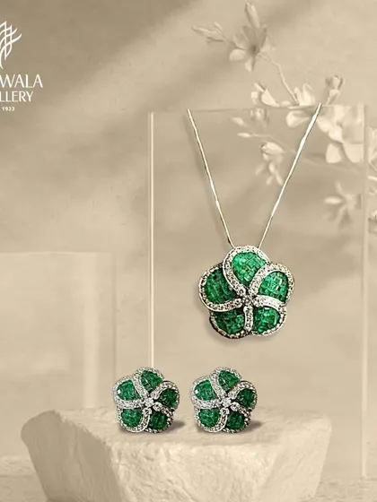 A beautiful floral pendant and earring set, crafted with green enamel and diamonds, displayed on a stone pedestal.
