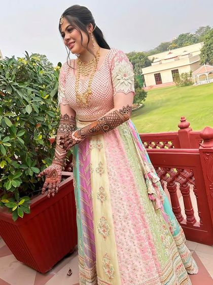 A beautiful bride in a pastel lehenga, showing off her full-arm bridal mehndi. The design looks stunning with her elegant outfit.
