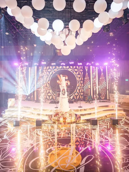 This is the moment. The cake cutting for Shivani and Nikhil, surrounded by our bespoke production. You can see the custom monogrammed dance floor, the multi-level stage, the orb centerpiece lighting, and perfectly timed pyrotechnics. We design every element to build up to these peak moments of celebration.