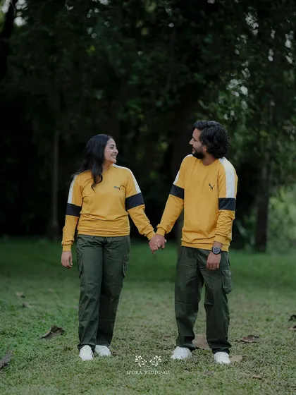 The couple holding hands and walking through a green field, a classic and romantic pre-wedding shot.