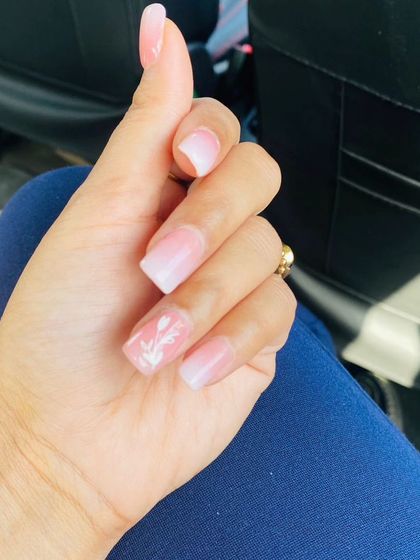 A soft pink and white ombre manicure with a delicate, hand-painted white floral design on an accent nail.
