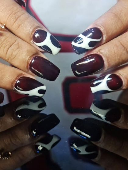 A chic and modern design with a deep burgundy base, featuring abstract white swirl patterns on accent nails.