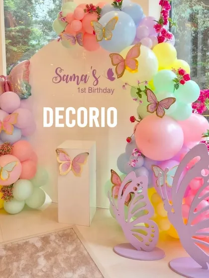A whimsical butterfly-themed first birthday party, perfect for a magical celebration. The decor features a pastel rainbow balloon arch over a personalized backdrop, accented with delicate butterfly cutouts and fresh flowers.