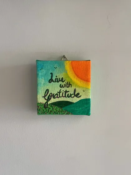 'Live with Gratitude'. This hand-painted mini canvas captures a simple, sunny landscape to serve as a daily reminder to appreciate the small joys in life. It's a little piece of sunshine for your wall.
