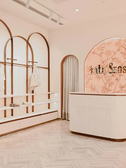 At Kate & Oscar, the customer journey begins at this welcoming reception desk. The curved form is set against a custom-illustrated backdrop, with arched clothing racks framing the space and hinting at the whimsical, gentle aesthetic of the store.