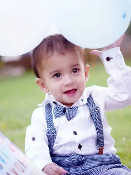 A sweet portrait of a baby boy holding up two white balloons during his outdoor photoshoot, with the soft green grass as a backdrop.