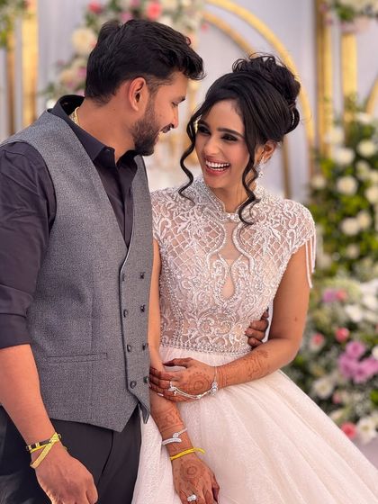 A happy couple at their reception. The bride is wearing a beautiful white gown with intricate beadwork, and her makeup is elegant and timeless.