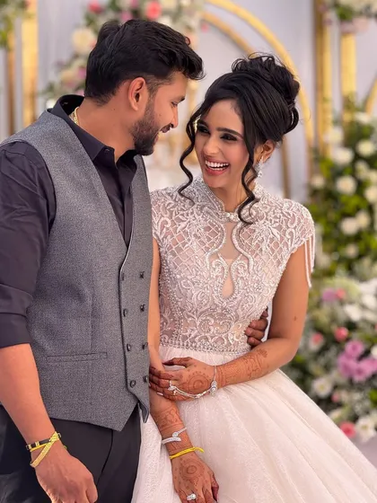 A happy couple at their reception. The bride is wearing a beautiful white gown with intricate beadwork, and her makeup is elegant and timeless.