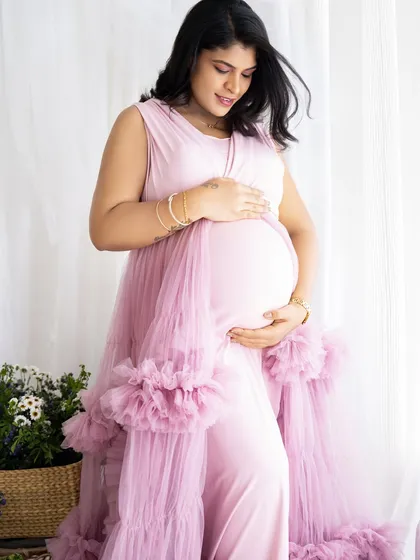 A gentle close-up of a mom-to-be cradling her bump, dressed in a lovely pink gown with ruffled details.