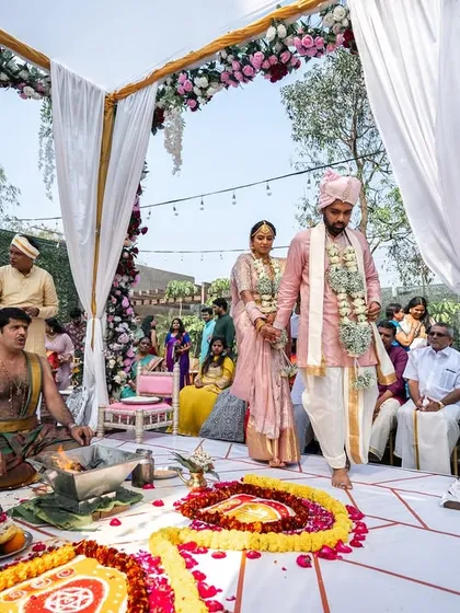 The couple taking their first steps as husband and wife around the sacred fire. The open-air mandap with floral decor creates a beautiful setting for this pivotal moment.