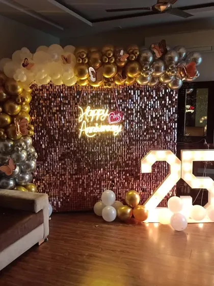 Celebrating a 25th anniversary in style. This rose gold sequin wall is decorated with a gold and silver balloon arch and a "Happy Anniversary" neon sign.