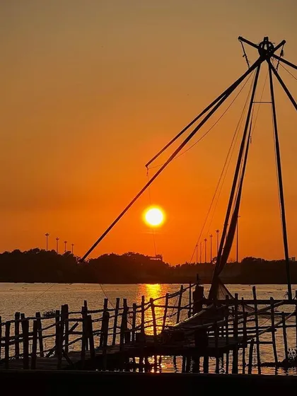 The iconic Chinese fishing nets of Kochi, Kerala, silhouetted against a warm sunset. This image captures a timeless tradition and the tranquil beauty of the backwaters, a story of culture meeting the coastline.