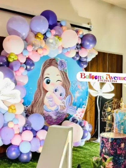 A detailed shot of a mermaid party backdrop, featuring a cute mermaid character and a vibrant balloon arch in shades of purple and pink.