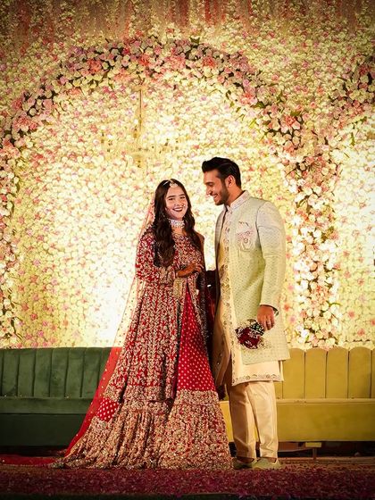 A happy, candid moment between the couple on their reception stage. The stunning wall of flowers creates a perfect backdrop for their joy.