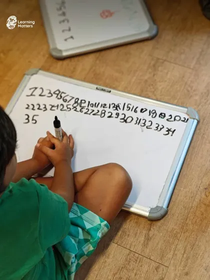 A child practices writing numbers on a whiteboard. We see this not as a test, but as a developmental stage. Reversed numbers and uneven lines are milestones, showing a brain that is learning to coordinate hand, eye, and an understanding of symbols.
