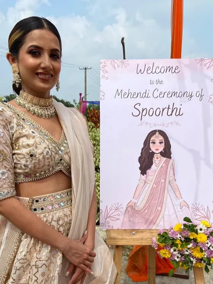 The beautiful bride poses next to her personalized welcome sign at her colorful Mehendi ceremony.