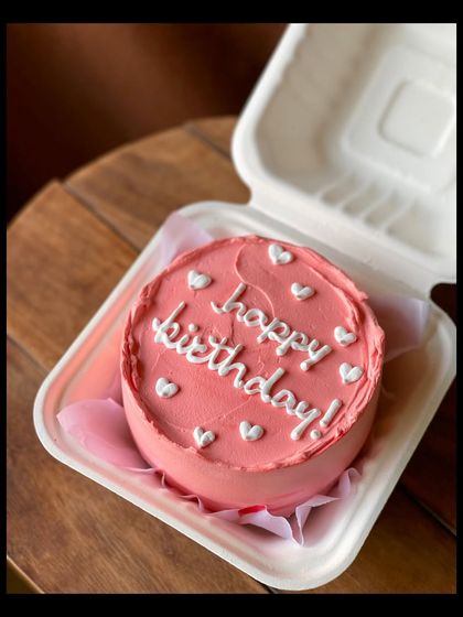 A lovely pink birthday bento cake with "happy birthday!" written in white, surrounded by little white hearts. It's simple, sweet, and perfect for any celebration.