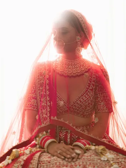 An artistic, backlit bridal portrait, with the bride's silhouette visible through her red veil.