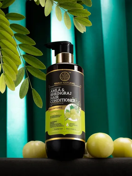 A hair conditioner bottle shot against a rich, green curtain with amla fruits. The deep colors and dramatic lighting give this natural product a luxurious and premium feel.