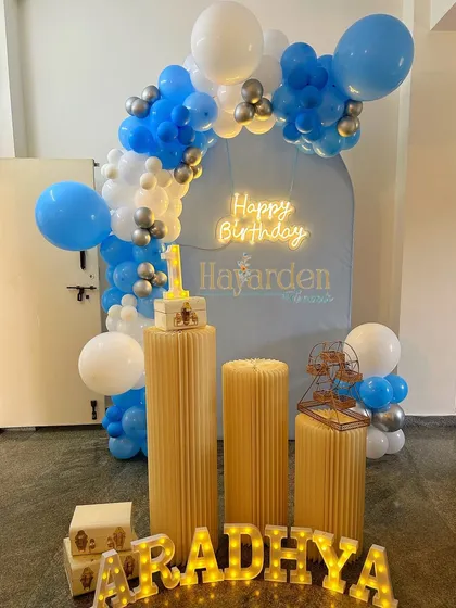A blue arched backdrop with a neon sign and a blue and white balloon garland.