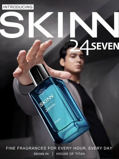 A commercial product shot for Skinn by Titan's fragrance line. The composition uses forced perspective to make the bottle the hero, while the model in the background provides a human element.