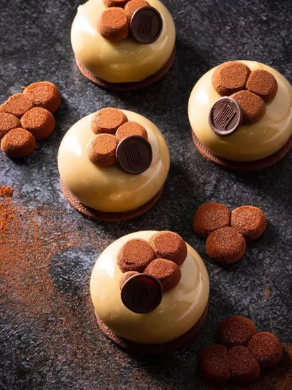 A dark and moody flat lay of several mini desserts from House of Amel. The dramatic lighting creates deep shadows that make the glossy glaze on the cakes stand out.