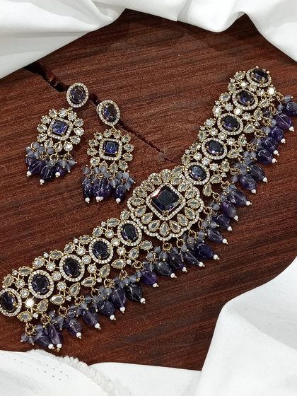 A versatile choker set available in multiple colors including white pearl, ruby, emerald, and pastel pink. The design features a central square motif with hanging beads, making it a popular choice for various festive occasions.