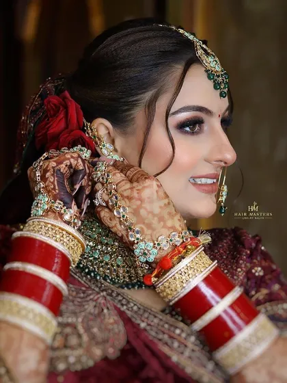 A detailed shot of the bride adjusting her earring. This highlights the side profile, the intricate hairstyle, and the beautiful coordination of her makeup with her jewelry.