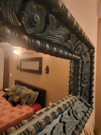 An ornate, hand-carved mirror with a distressed finish adds a touch of vintage charm and reflects the warm, earthy tones of this bedroom.