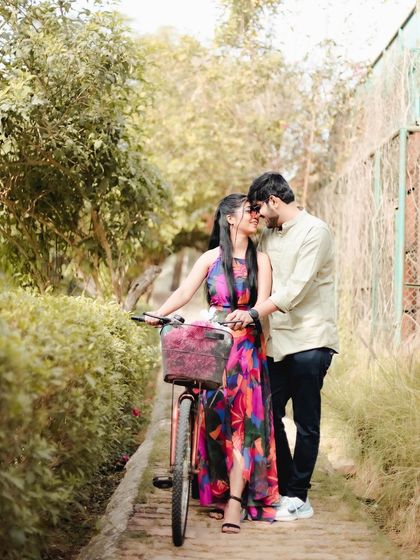 A romantic moment captured on a narrow garden path, with the couple sharing a kiss next to a bicycle. The lush greenery creates a private and intimate setting for this pre-wedding photo.