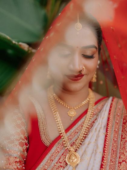 An artistic shot through the veil. The focus is on her beautifully done eye makeup and the bold red lip, which are key elements of her traditional bridal look.