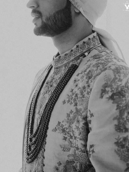 A detailed black and white shot of the groom's profile, highlighting the texture of his beard and the intricate embroidery on his sherwani. A classic and masculine portrait.