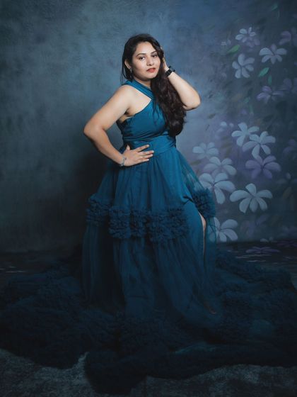 A full-length portrait showcasing the dramatic flow of a teal maternity gown as the mother-to-be poses elegantly.